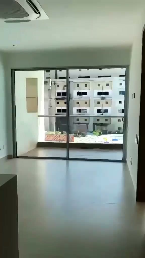 Sala vacía en obra gris, con puerta de vidrio al balcón, tal como la entrega el constructor