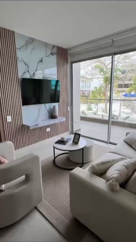 Sala dotada por Reddy con muro de listones y mármol, televisor, sofá y mesa de centro